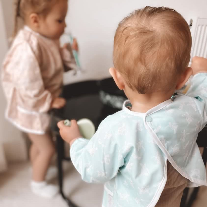 Child wearing a light blue bib looking at themselves in a mirror.