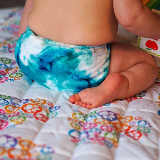 Baby in a blue minky cloth nappy sitting on a Baby Bare playmat reverse side with heart logo