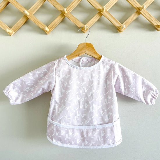 Pink baby feeding smock featuring blossoms on a hanger