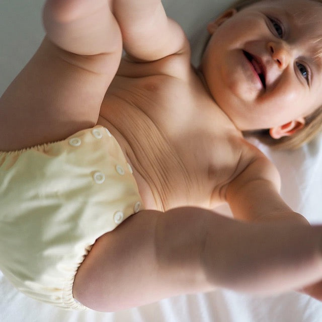 Smiling baby wearing a butter yellow cloth nappy
