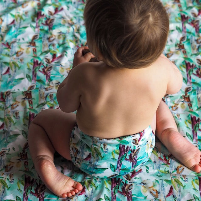 Baby sitting on a change mat featuring kookaburras wearing a matching cloth nappy