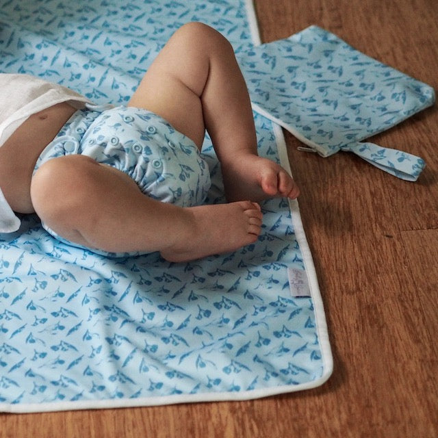 A baby lying on a blue change mat wearing a matching nappy