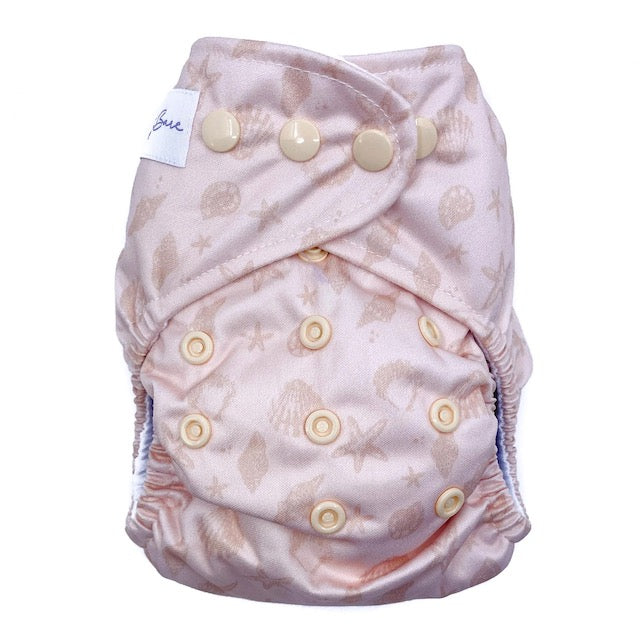 A reusable cloth nappy with a sea shell print on a pink base