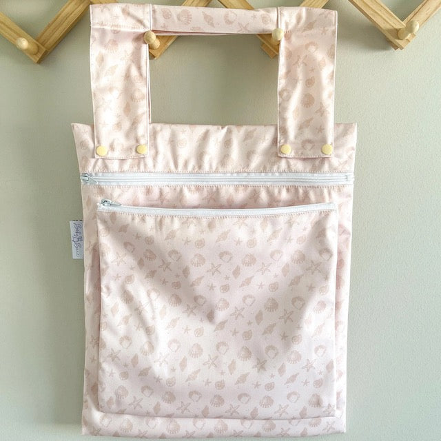 A pink double wet bag with a sea shell design on a hanger