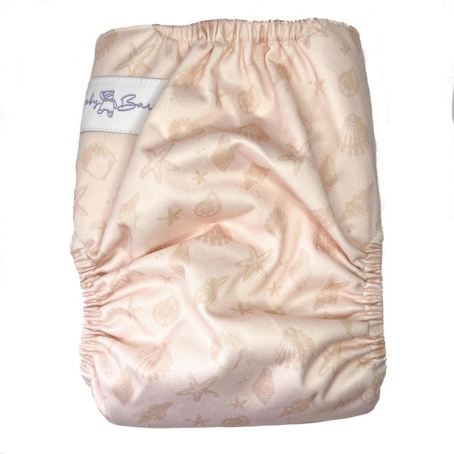 A reusable cloth nappy with a sea shell print on a pink base