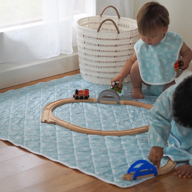 Children playing on a turquoise play mat with a wooden train set
