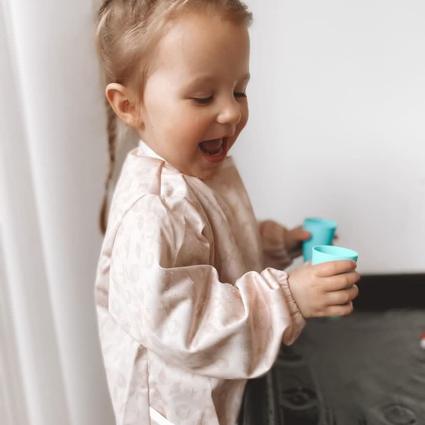 Little girl wearing a pink smock playing with water