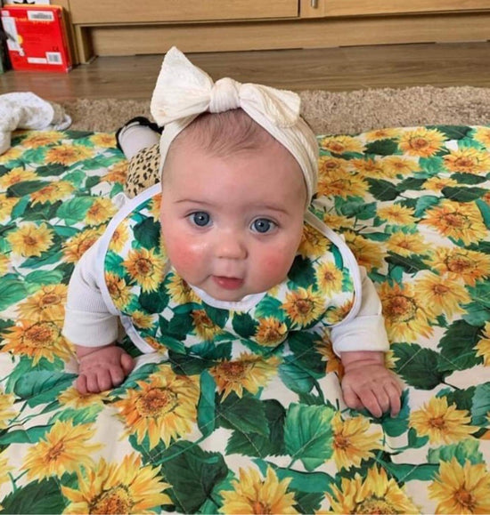 Baby on a play mat wearing a sunflower print bib