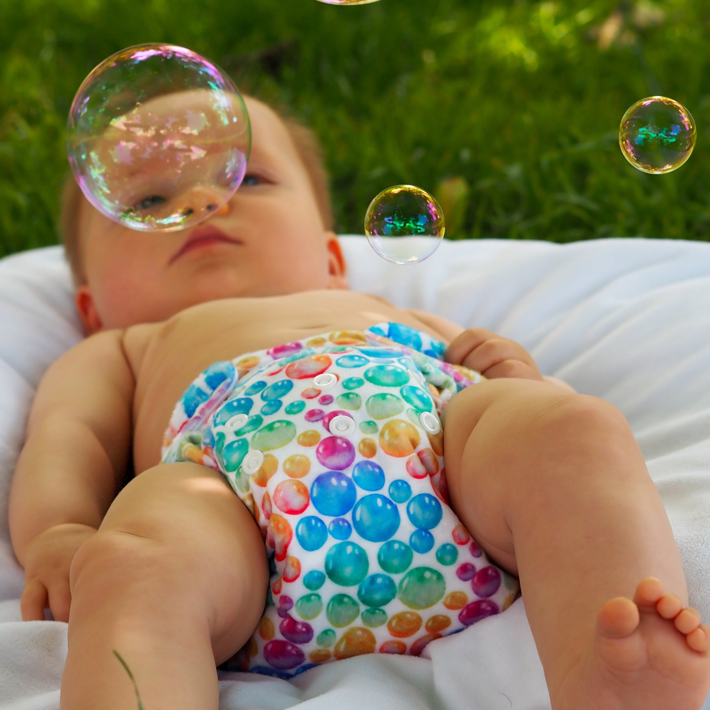Baby looking at bubbles wearing a colourful bubble print cloth nappy