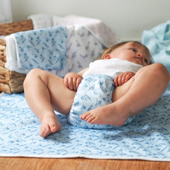 A baby lying on a blue change mat wearing a matching nappy