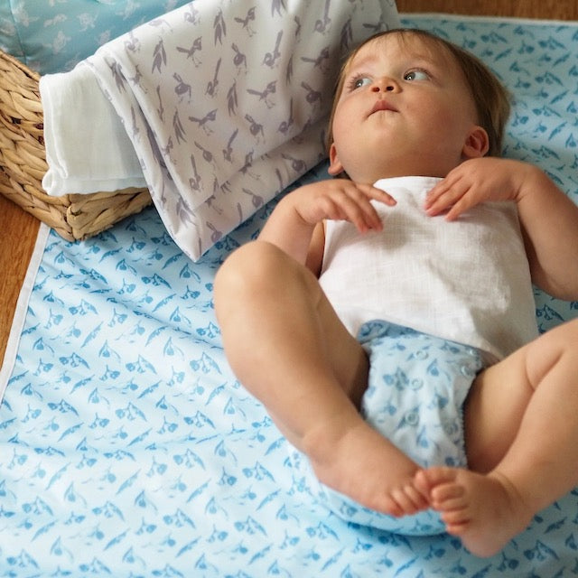 A baby lying on a blue change mat wearing a matching nappy