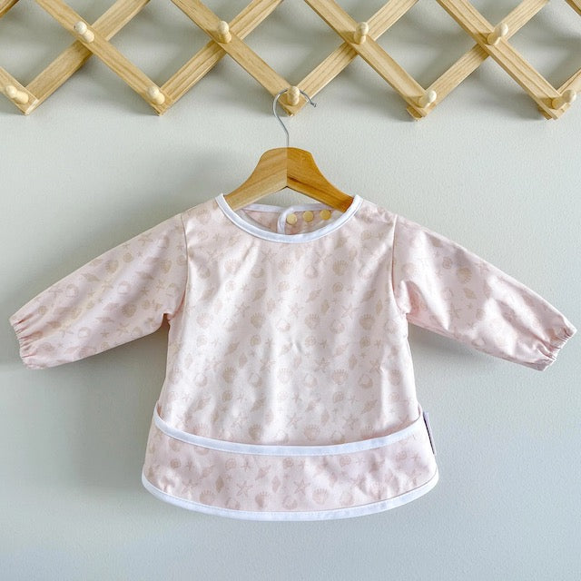 Pink baby feeding smock featuring sea shells on a hanger