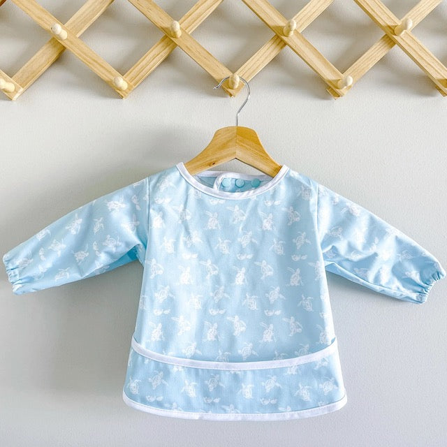 Blue baby feeding smock featuring turtles on a hanger