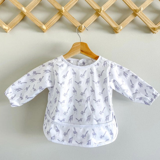 White baby feeding smock featuring lilac wrens on a hanger